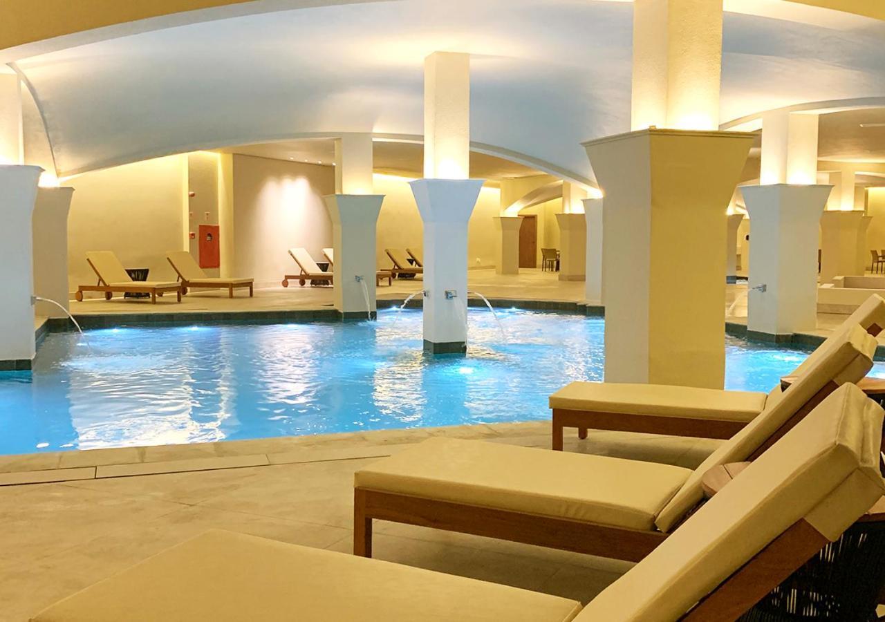 Buona Vitta Gramado Resort & Spa By Gramado Parks Екстер'єр фото The photo shows an indoor spa or relaxation area with a tranquil atmosphere. There is a large swimming pool with clear blue water, illuminated by soft lighting. Surrounding the pool are several comfortable lounge chairs. The architecture features ele