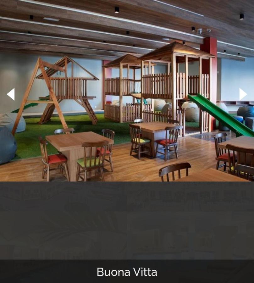 Buona Vitta Gramado Resort & Spa By Gramado Parks Екстер'єр фото The photo shows a play area designed for children, featuring a wooden play structure with slides and climbing areas. In the foreground, there are several small wooden tables and chairs arranged for seating. The floor is covered with green turf, resem