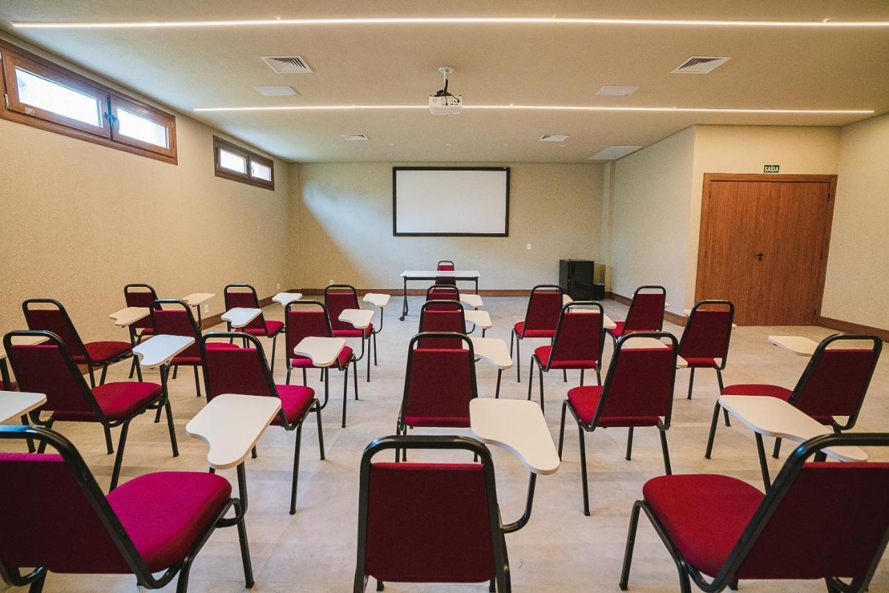 Buona Vitta Gramado Resort & Spa By Gramado Parks Екстер'єр фото The photo shows a classroom or meeting room set up for a presentation or lecture. It features several rows of red chairs, each with a small writing surface attached. There is a blank screen mounted on the wall at the front of the room, likely for dis