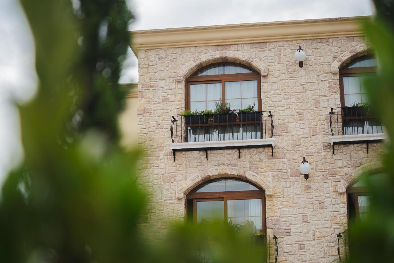 Buona Vitta Gramado Resort & Spa By Gramado Parks Екстер'єр фото The photo depicts a stone building with a textured exterior. It features several windows with wooden frames. Each window has a small balcony adorned with decorative plants. There are also wall-mounted light fixtures flanking the windows. In the foreg