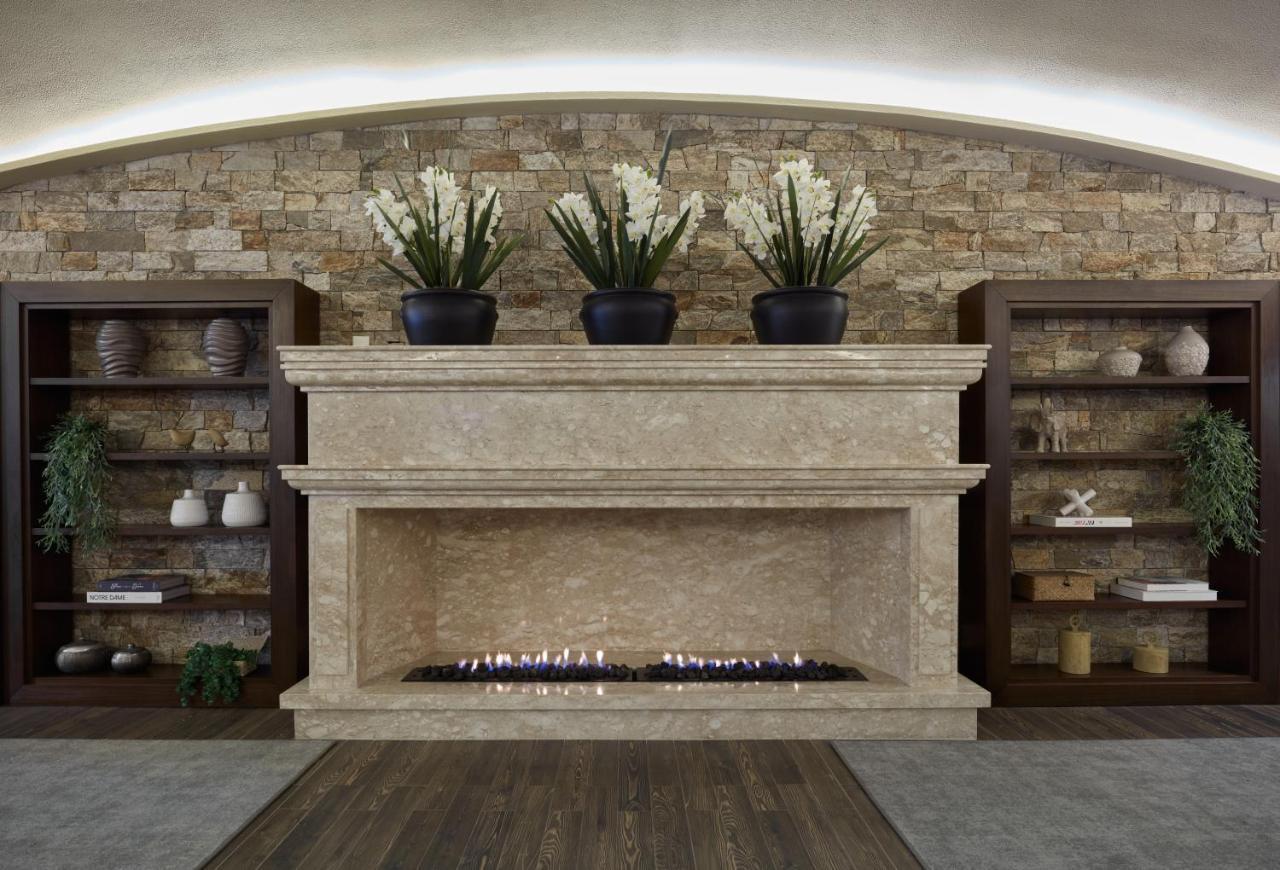 Buona Vitta Gramado Resort & Spa By Gramado Parks Екстер'єр фото The photo shows a modern fireplace design built into a wall with a textured stone background. The fireplace is made of a light-colored stone and features a long, narrow gas flame visible at the bottom. Above the fireplace, there are two large potted 
