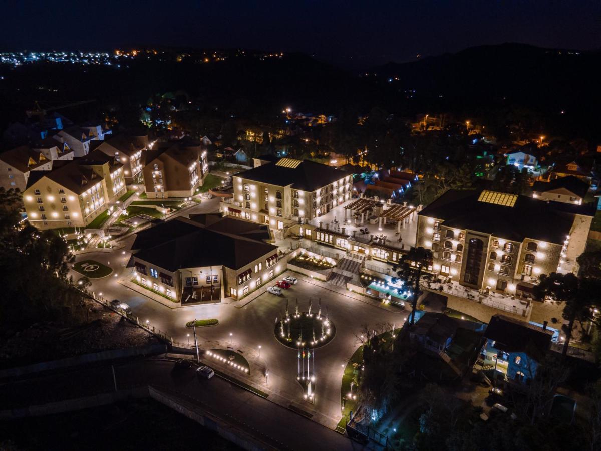 Buona Vitta Gramado Resort & Spa By Gramado Parks Екстер'єр фото The photo shows a beautifully lit resort or hotel complex taken at night. The buildings are well-illuminated, highlighting their architecture. There is a circular area with a fountain at the center, surrounded by pathways that connect various parts o