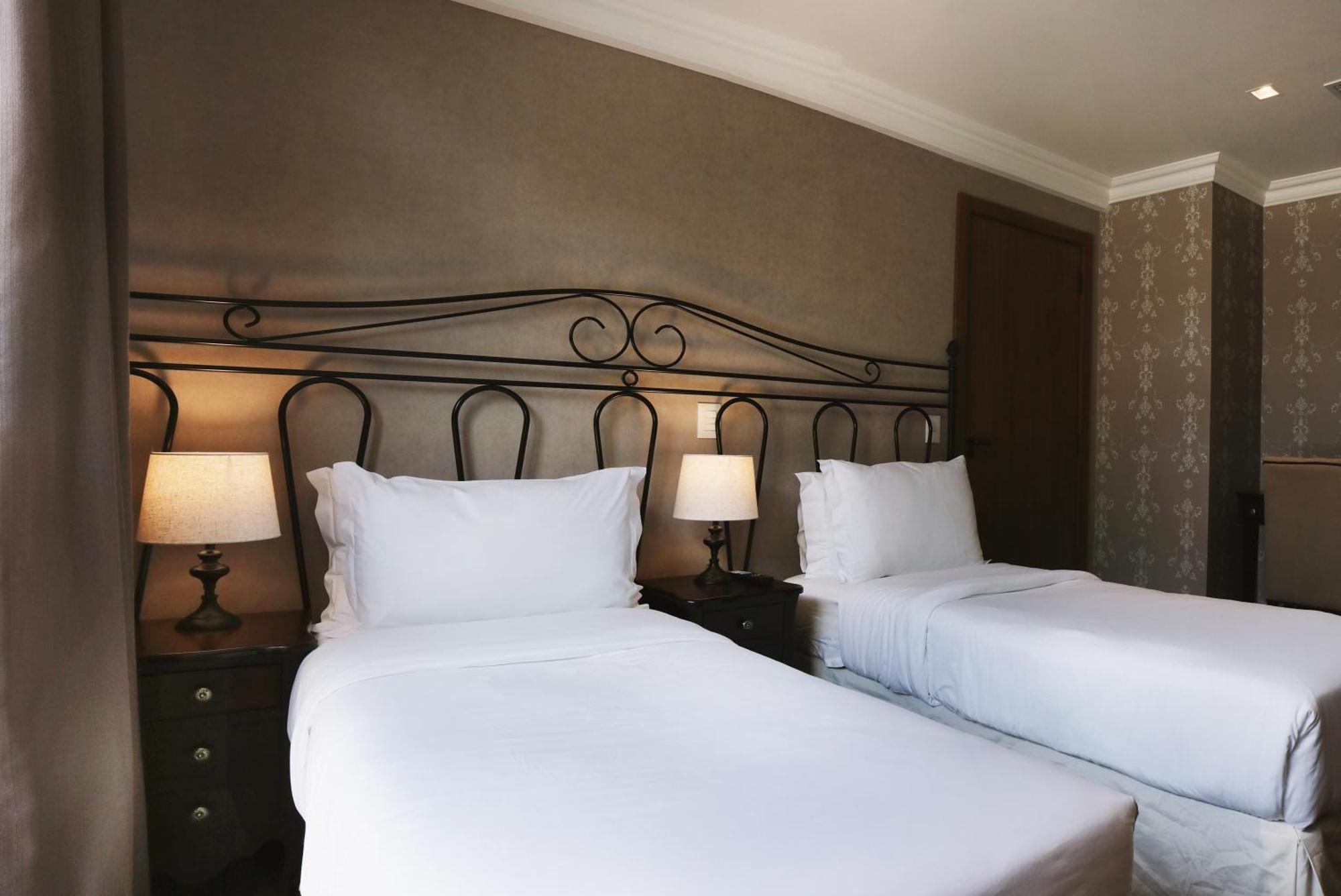 Buona Vitta Gramado Resort & Spa By Gramado Parks Екстер'єр фото The photo shows a neatly arranged hotel room featuring two single beds with white bedding. The beds have decorative metal headboards, and there are bedside tables on either side with lamps. The room's walls have a subtle design, and there is a door v