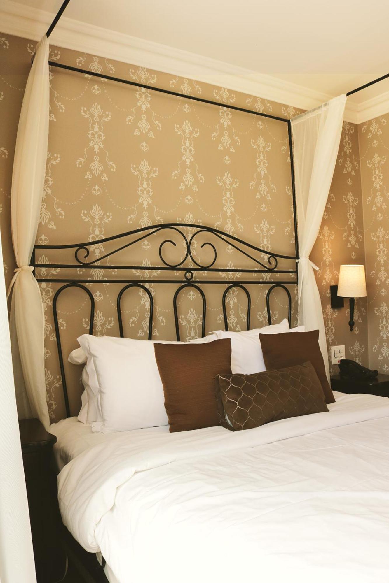Buona Vitta Gramado Resort & Spa By Gramado Parks Екстер'єр фото The photo shows a cozy bedroom setup featuring a decorative metal bed frame with a scroll design as the headboard. The bed is adorned with several white pillows and two brown decorative cushions. The wall behind the bed is covered with a light-colore