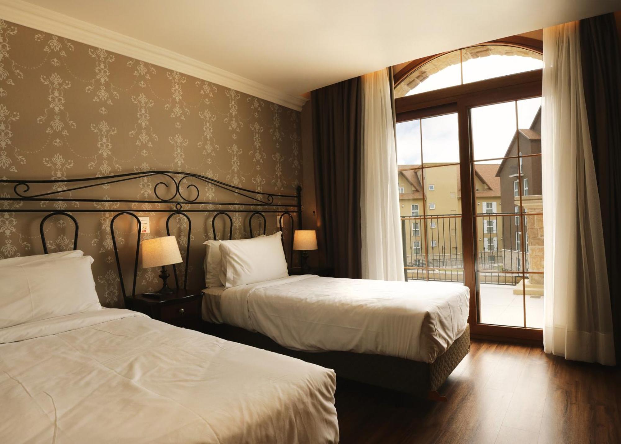 Buona Vitta Gramado Resort & Spa By Gramado Parks Екстер'єр фото The photo shows a well-decorated hotel room featuring two beds. One bed is larger, likely a double bed, while the other is a single bed. The walls are adorned with a floral pattern, and there are bedside lamps next to the larger bed. Large windows wi