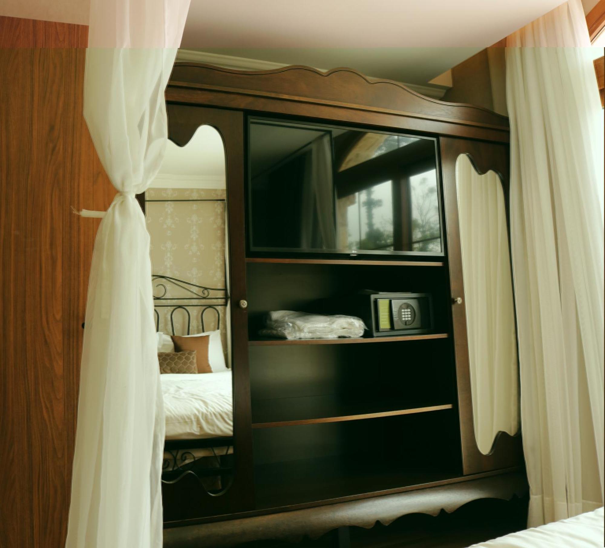 Buona Vitta Gramado Resort & Spa By Gramado Parks Екстер'єр фото The image shows a wooden cabinet with a television mounted on the front. The cabinet has decorative edges and is paired with sheer white curtains on either side. Inside the cabinet, there are shelves, and a small safe or storage box is visible on one