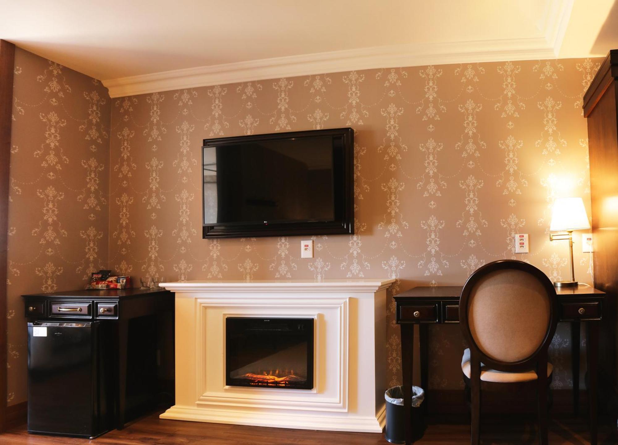 Buona Vitta Gramado Resort & Spa By Gramado Parks Екстер'єр фото The photo shows a cozy room featuring a decorative wall with a subtle pattern. On one side, there is a modern flat-screen television mounted on the wall. Below it, there is a stylish electric fireplace framed in white. Adjacent to the fireplace is a 
