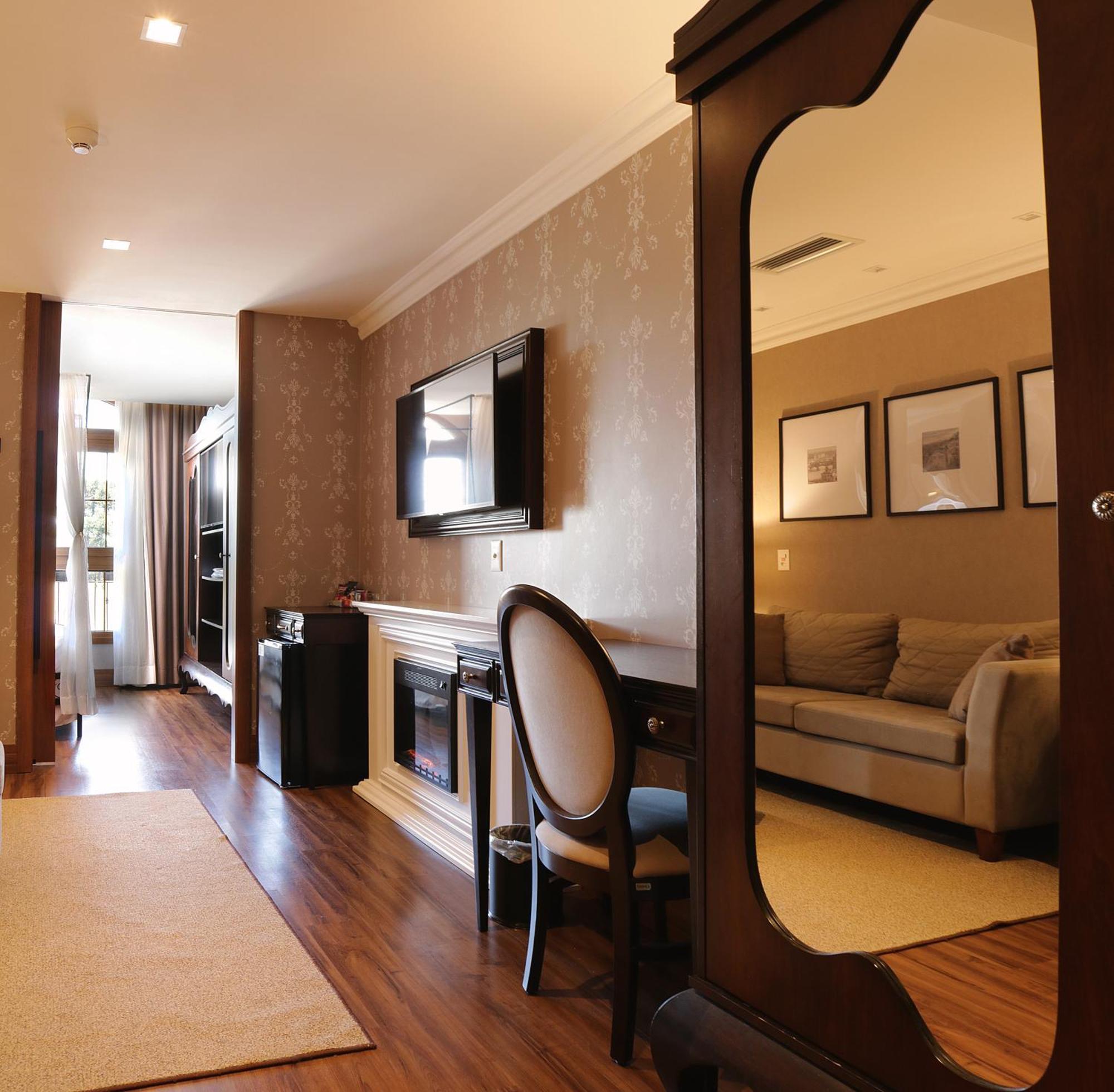 Buona Vitta Gramado Resort & Spa By Gramado Parks Екстер'єр фото The photo shows a well-decorated room that appears to be a living area or a hotel suite. In the foreground, there is a round chair and a desk. A large mirror reflects the living space, creating a sense of spaciousness. 

On the wall is a flat-screen 