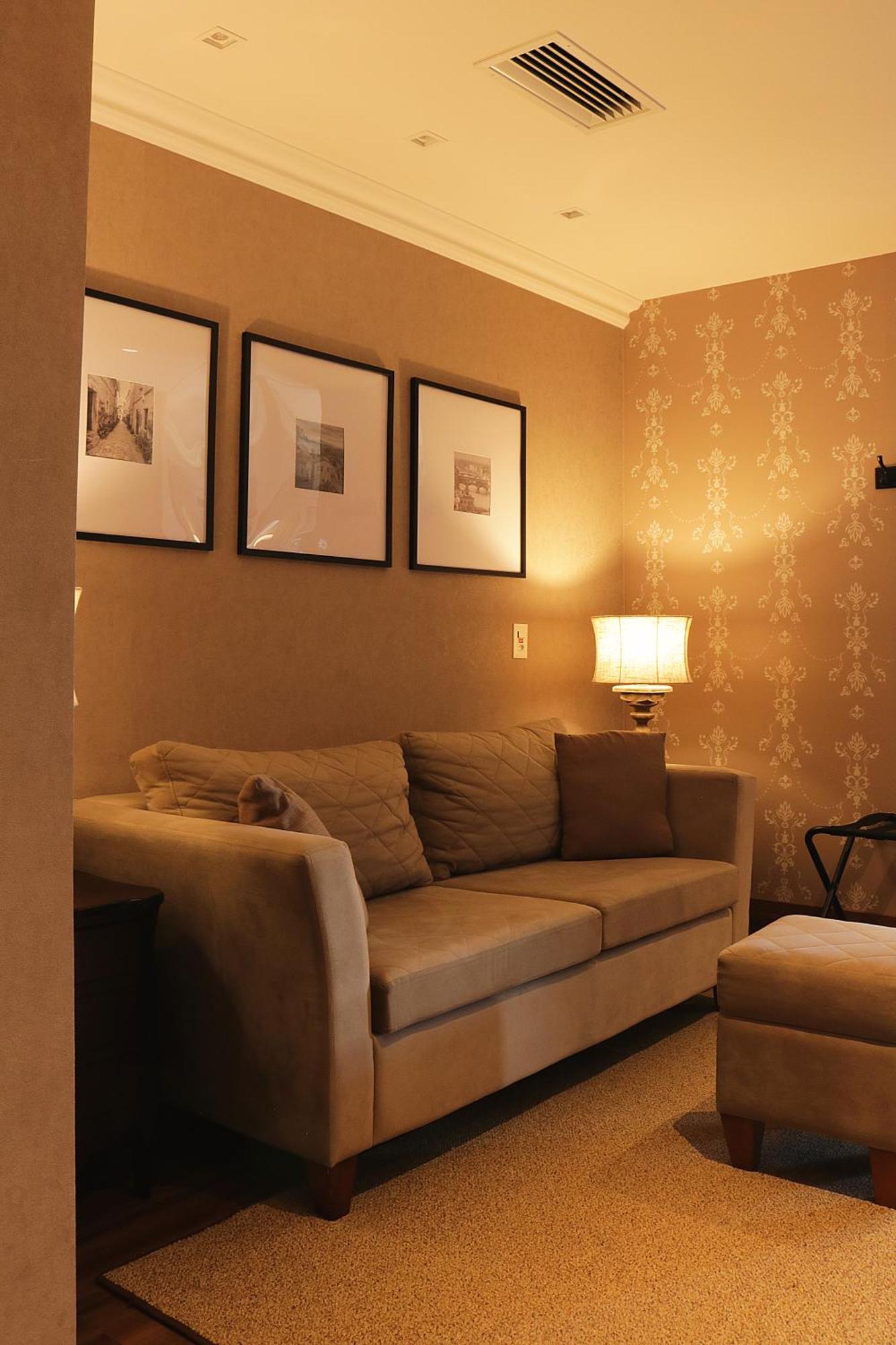 Buona Vitta Gramado Resort & Spa By Gramado Parks Екстер'єр фото The photo shows a cozy living room setting. There is a light-colored sofa adorned with several cushions, positioned against a wall that has a subtle pattern. Above the sofa, there are three framed artworks or photographs hanging on the wall. To the s