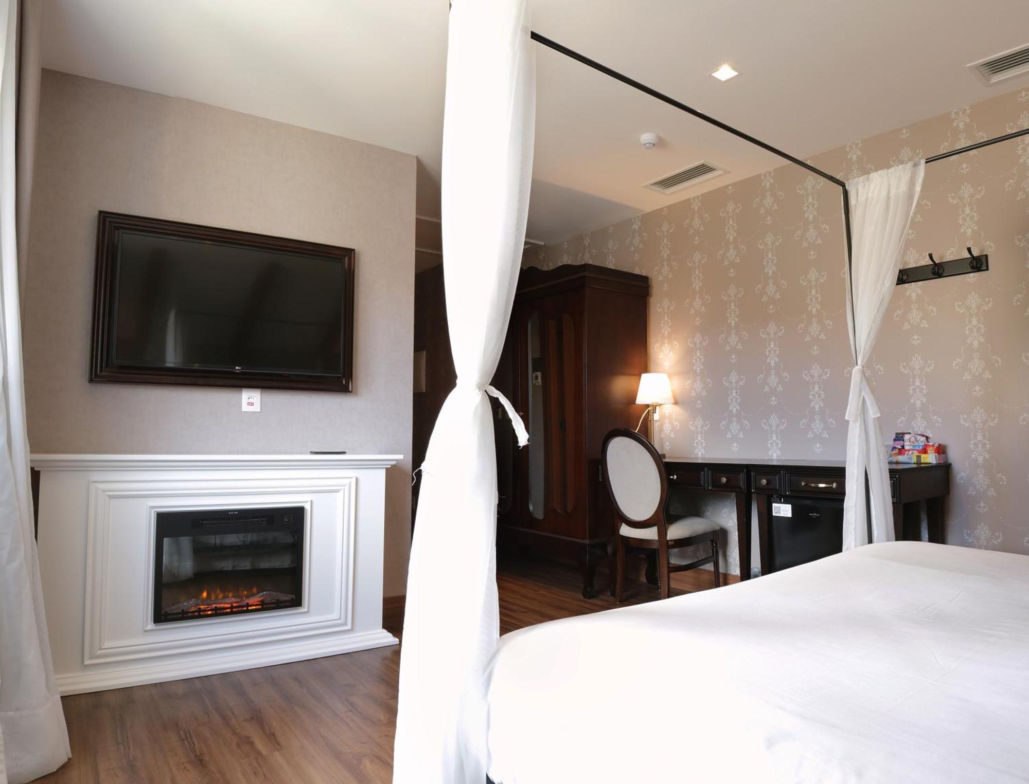Buona Vitta Gramado Resort & Spa By Gramado Parks Екстер'єр фото The photo shows a cozy hotel room with elegant decor. There is a white bed with a canopy, and a modern television mounted on the wall across from it. To the side, a fireplace is built into a white mantel, adding a warm touch to the space. There's a w